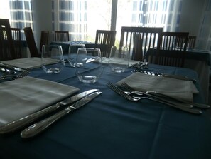 Una mesa de comedor lista con cubiertos y vasos, con sillas alrededor.