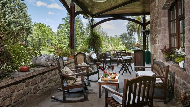 A covered patio with wooden furniture, stone walls, and a view of the garden. - El Jardín de Carrejo (Cabezon de la Sal)