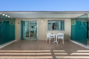 A covered outdoor seating area with a table and chairs, a sliding glass door leading to a room, and a tiled roof.