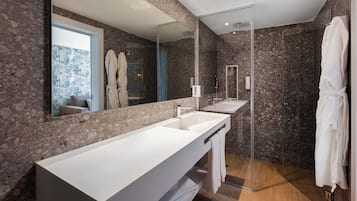 Un baño moderno con un espejo grande, un tocador blanco, una cabina de ducha de vidrio y una bata colgada en la pared.