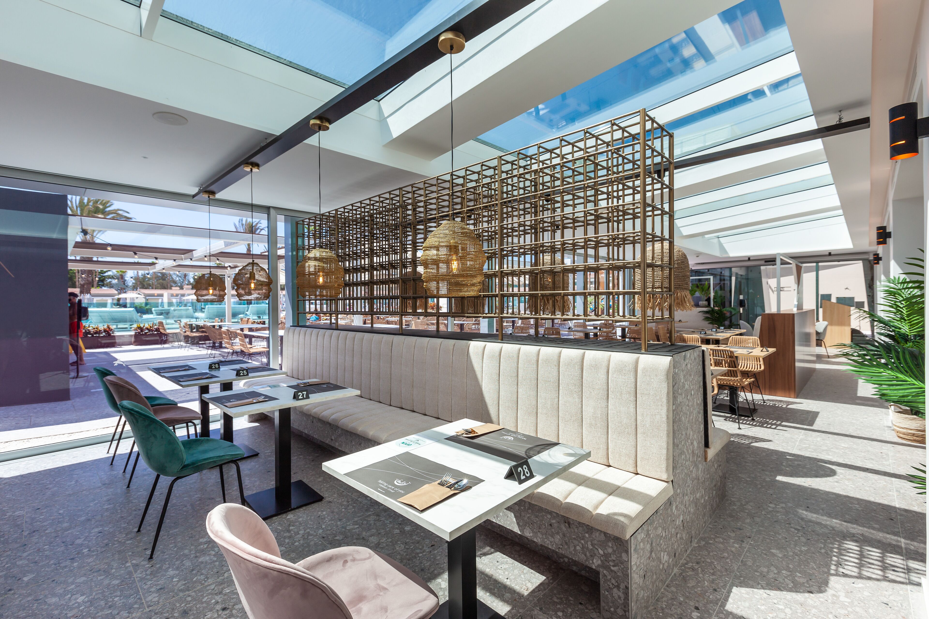A modern restaurant with a glass partition, outdoor seating, and a pool view.