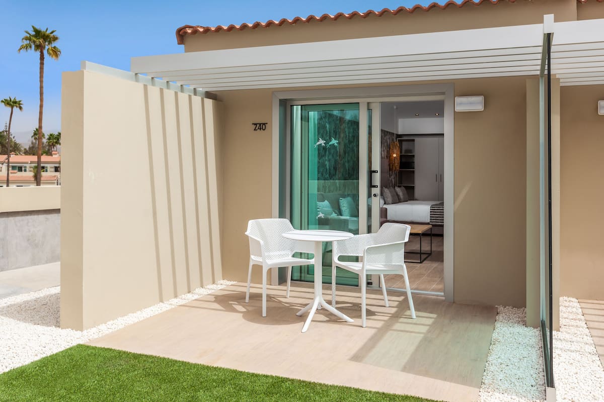 Une terrasse extérieure moderne, avec une porte vitrée donnant sur une pièce, des meubles blancs et une pelouse bien entretenue.