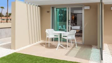A modern outdoor patio with a glass door leading to a room, white furniture, and a well-maintained lawn.