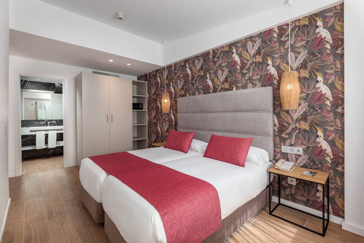 Une chambre à coucher avec un grand lit, une table de chevet avec une lampe, une armoire et une salle de bain visible à travers une porte ouverte.