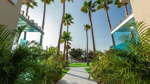 A pathway flanked by tall palm trees and lush greenery, leading to a building with a modern design and a blue accent wall. - Kumara Serenoa by Lopesan Hotels (San Bartolomé de Tirajana)