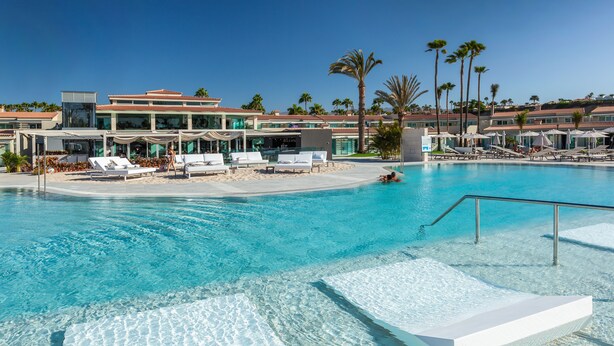 A clear blue pool with white lounge chairs and a palm tree-lined background. - Kumara Serenoa by Lopesan Hotels (San Bartolomé de Tirajana)
