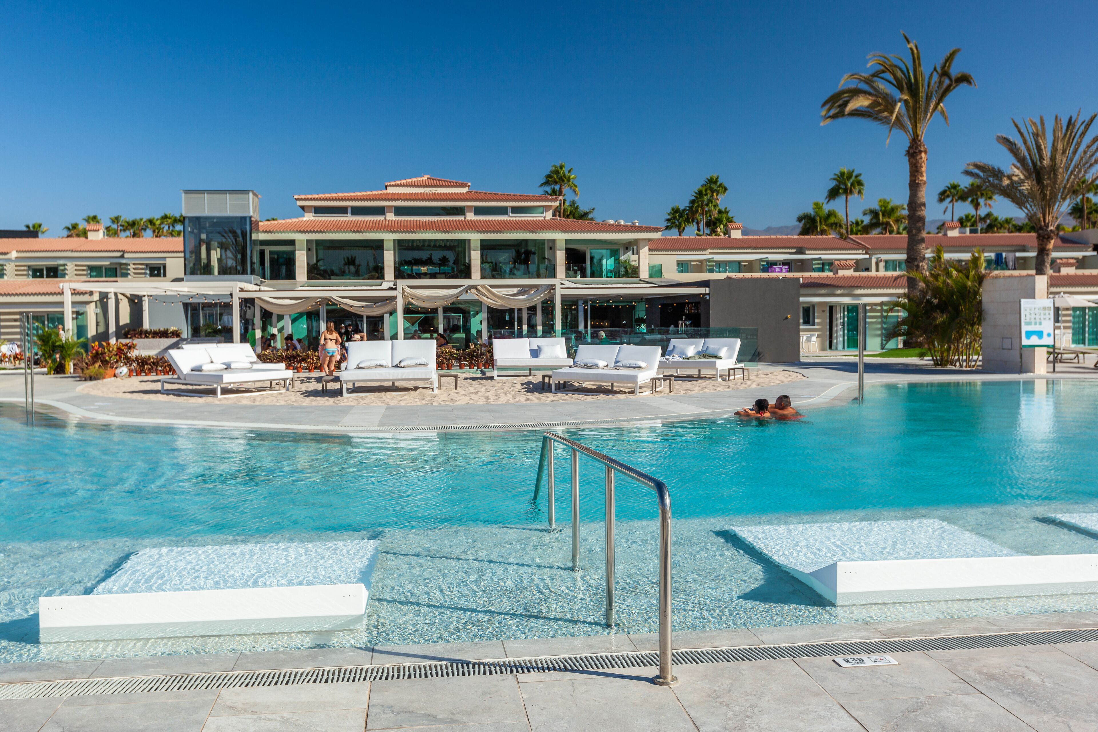 Ein Swimmingpool mit Liegestühlen und ein mehrstöckiges Gebäude mit Balkonen im Hintergrund.