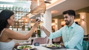 A couple toasting with wine glasses at a restaurant table with a number 22 sign, under a woven pendant light. - Kumara Serenoa by Lopesan Hotels (San Bartolomé de Tirajana)