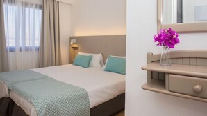 A hotel room with a bed, a bedside table with a vase of flowers, and a mirror above the table. - Los Tulipanes (Tias)