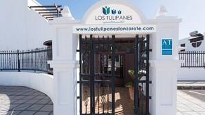 A gated entrance to a building with a sign reading "Los Tulipanes Apartamentos" and a website address. - Los Tulipanes (Tias)