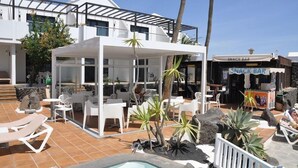 A pool area with lounge chairs, a covered seating area, and a snack bar. - Los Tulipanes (Tias)