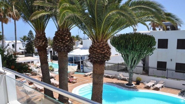 A pool area with palm trees, lounge chairs, and a clear blue pool. - Los Tulipanes (Tias)