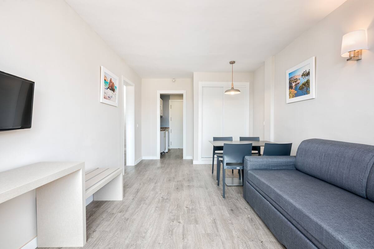 Ett modernt vardagsrum med en grå soffa, en TV som är monterad på väggen och en matplats med ett bord och stolar.