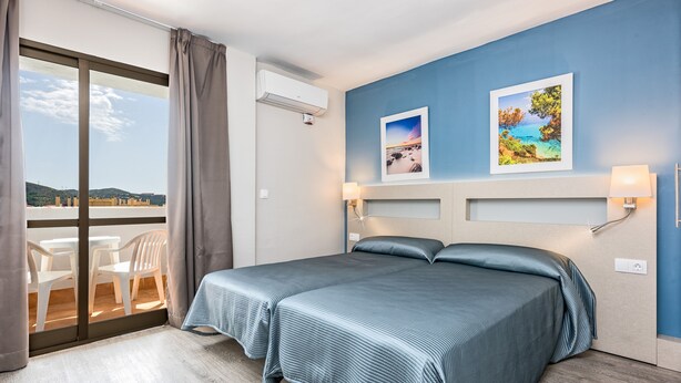 Une chambre d’hôtel avec un grand lit, un balcon avec des chaises et deux tableaux encadrés au mur.