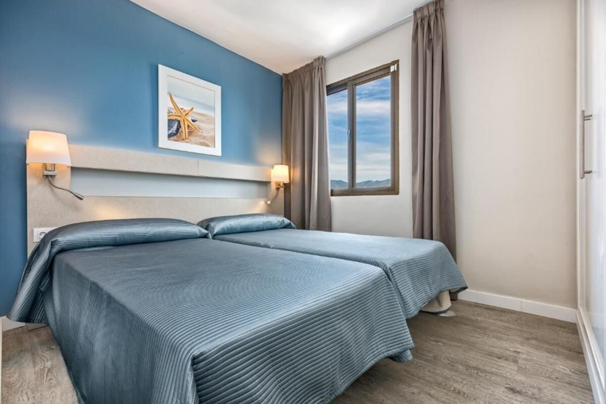 A hotel room with two beds, a large window with curtains, and a framed picture on the wall.
