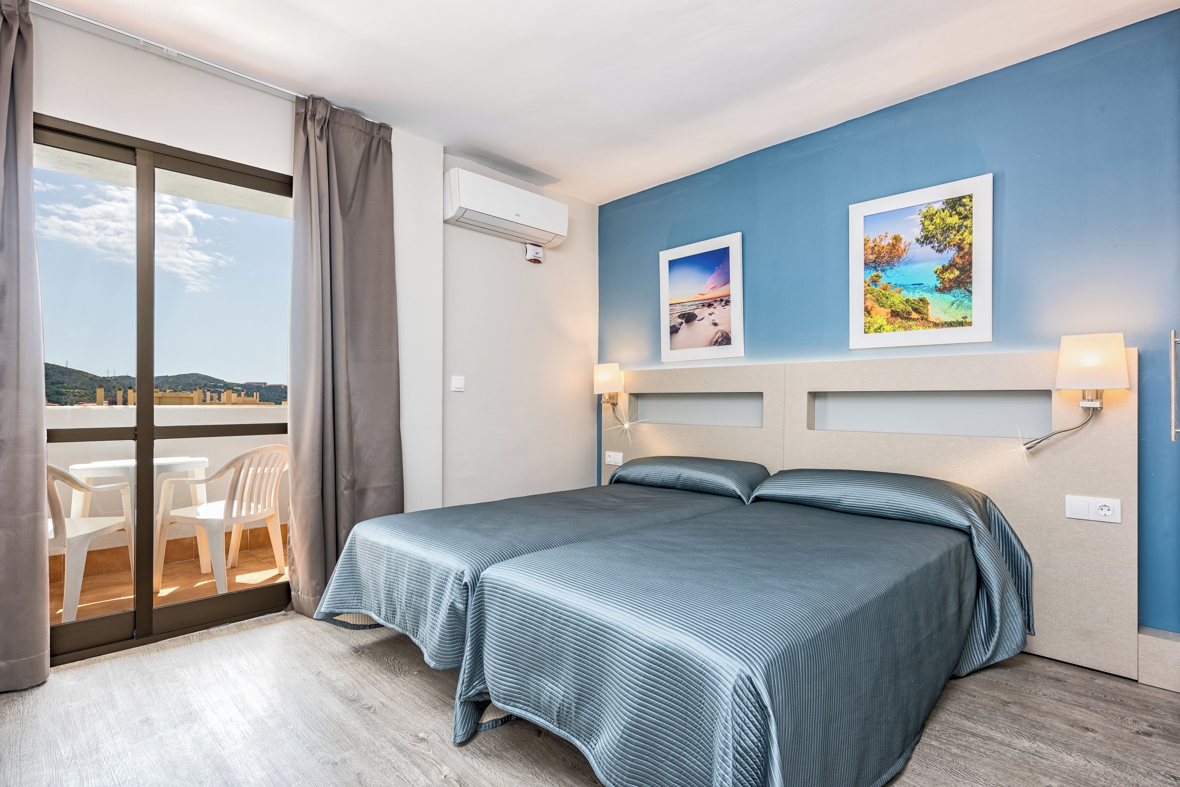 Una habitación de hotel con una cama, dos cuadros colgados en la pared, una ventana con cortinas y vistas al paisaje.