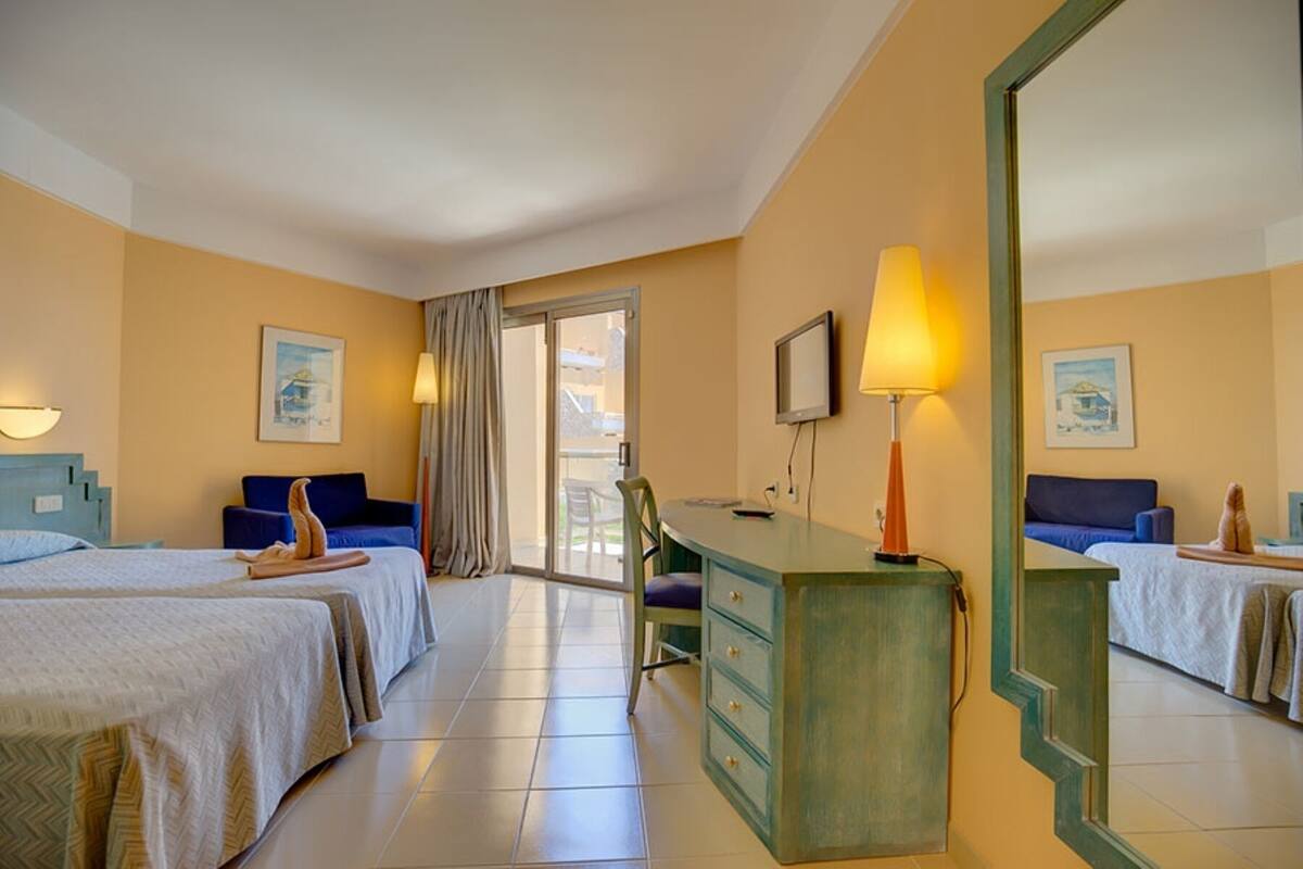 A hotel room with two beds, a desk, a chair, a TV, and a large mirror.