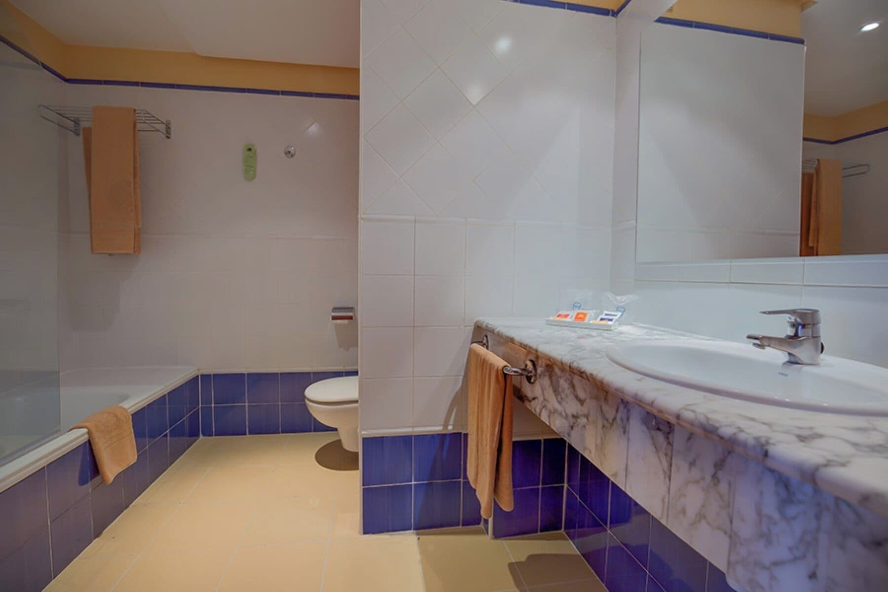 Et badeværelse med badekar, toilet og en håndvask med marmorplade.