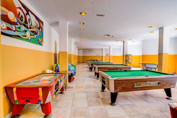 Una sala de billar con varias mesas de billar, un mural colorido y un suelo de baldosas.