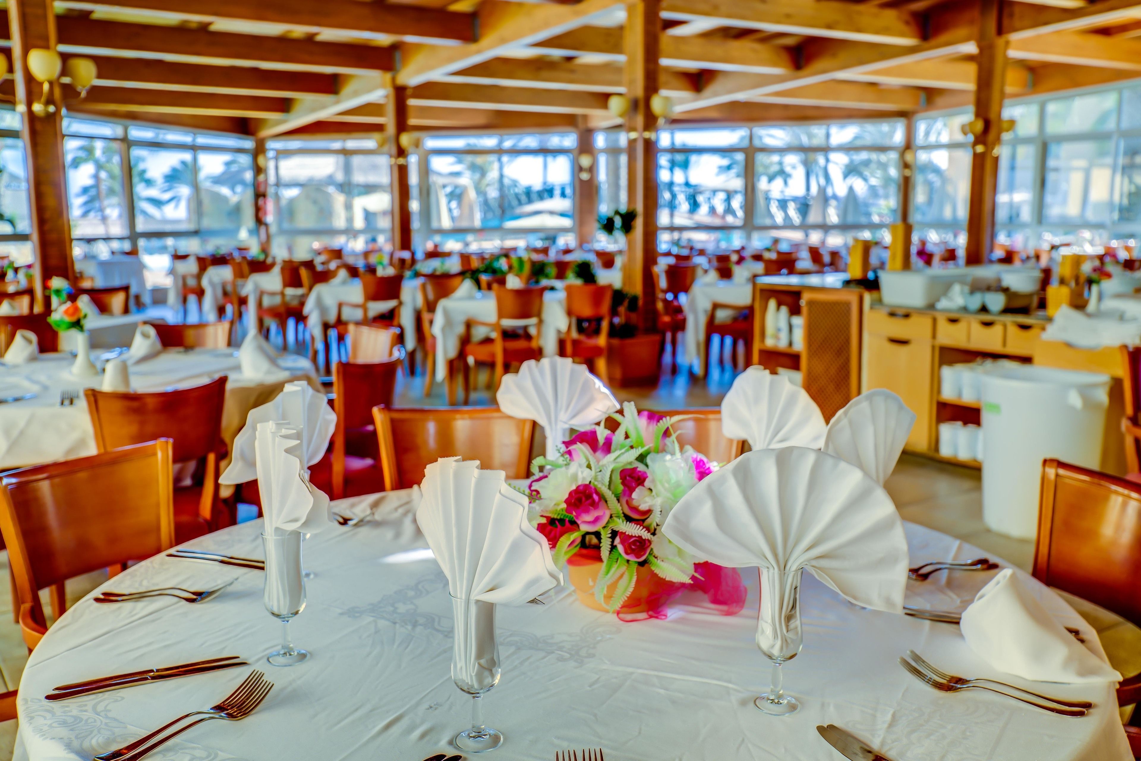 A restaurant with round tables set for dining, featuring white tablecloths, folded napkins, and glassware.