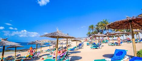 A beach with sun loungers and thatched umbrellas.