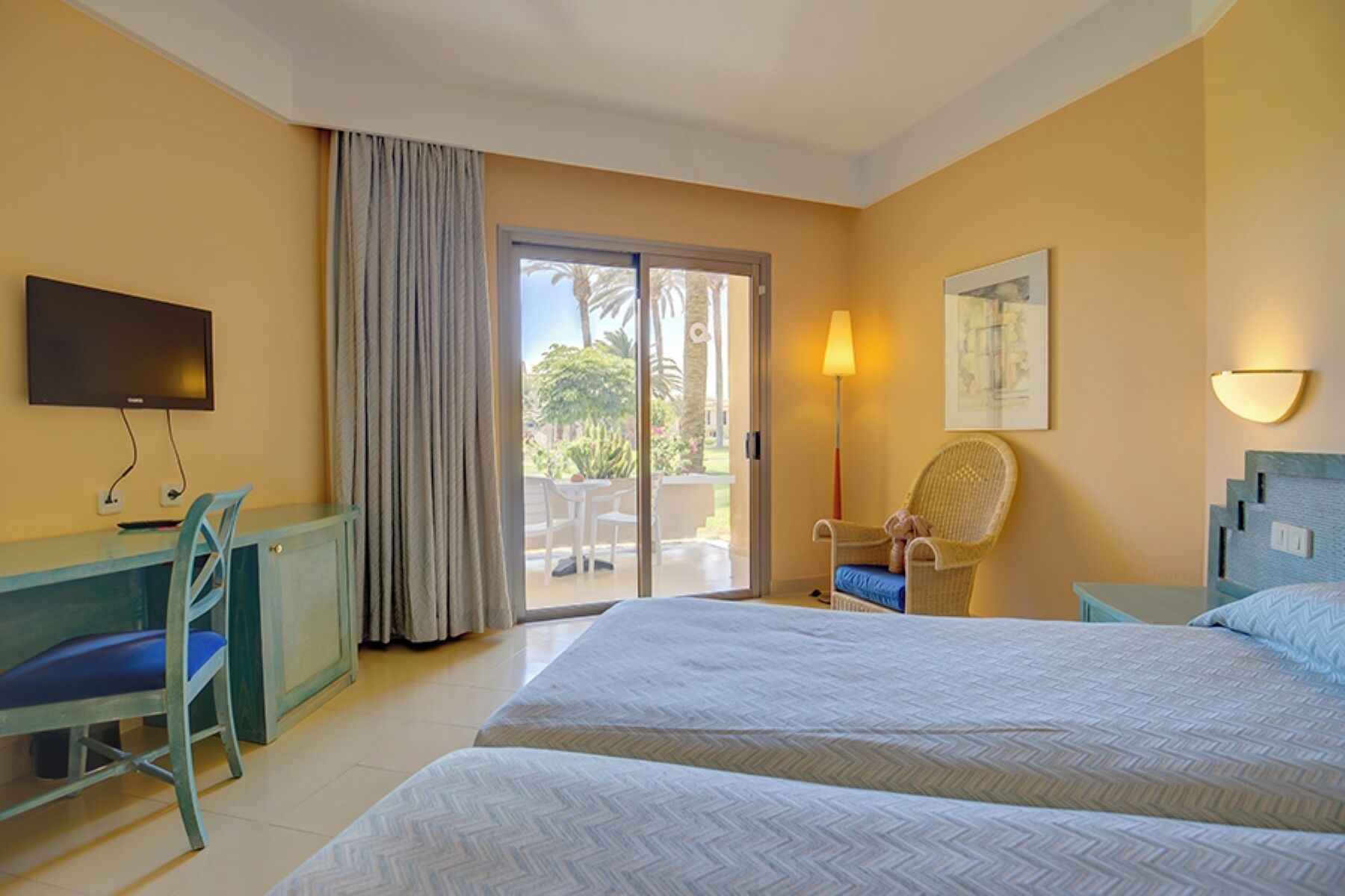 A hotel room with a bed, a desk, a chair, a TV, a lamp, and a view of the outdoors.