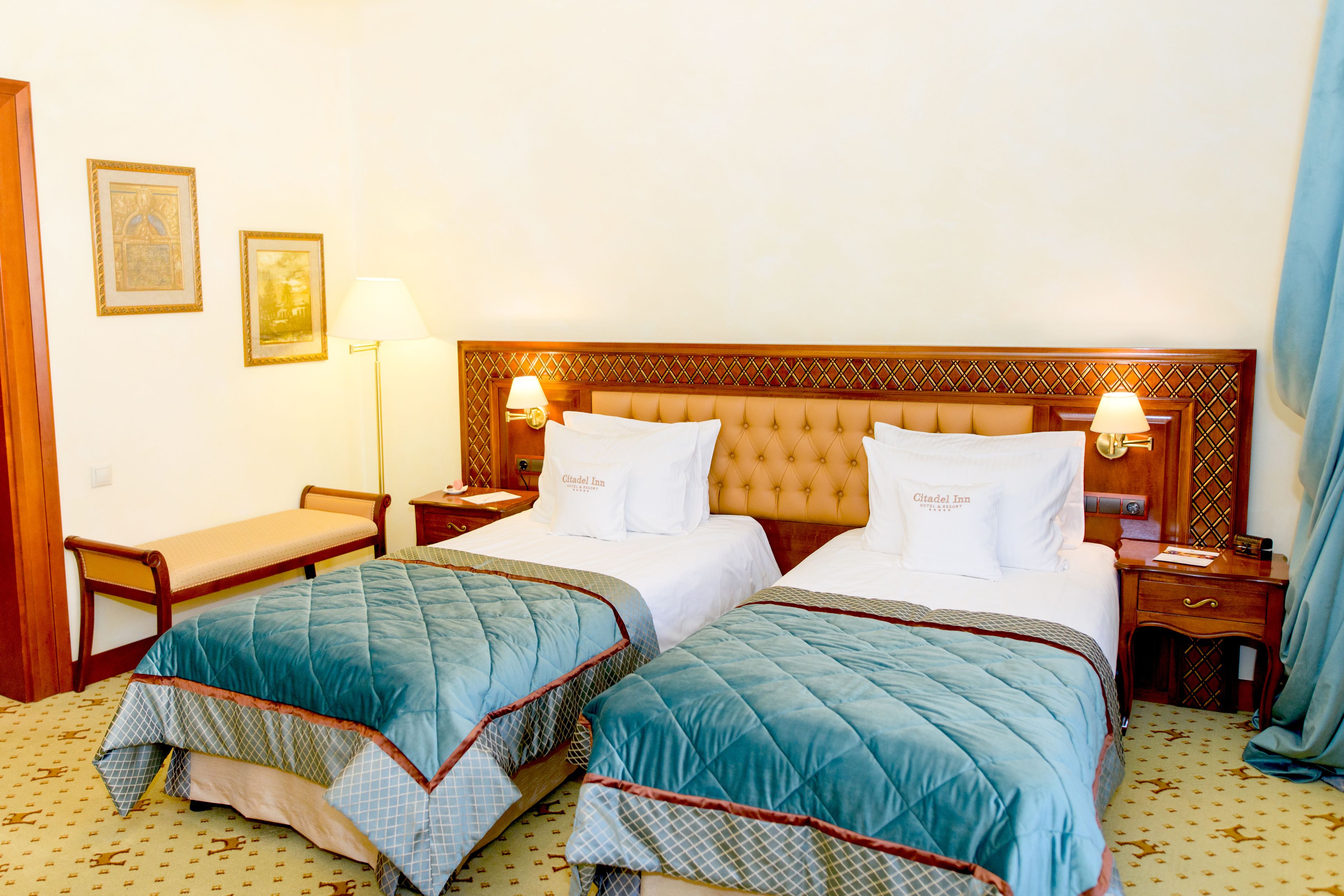 Una habitación de hotel con dos camas, un banco, una mesita de noche y una lámpara.