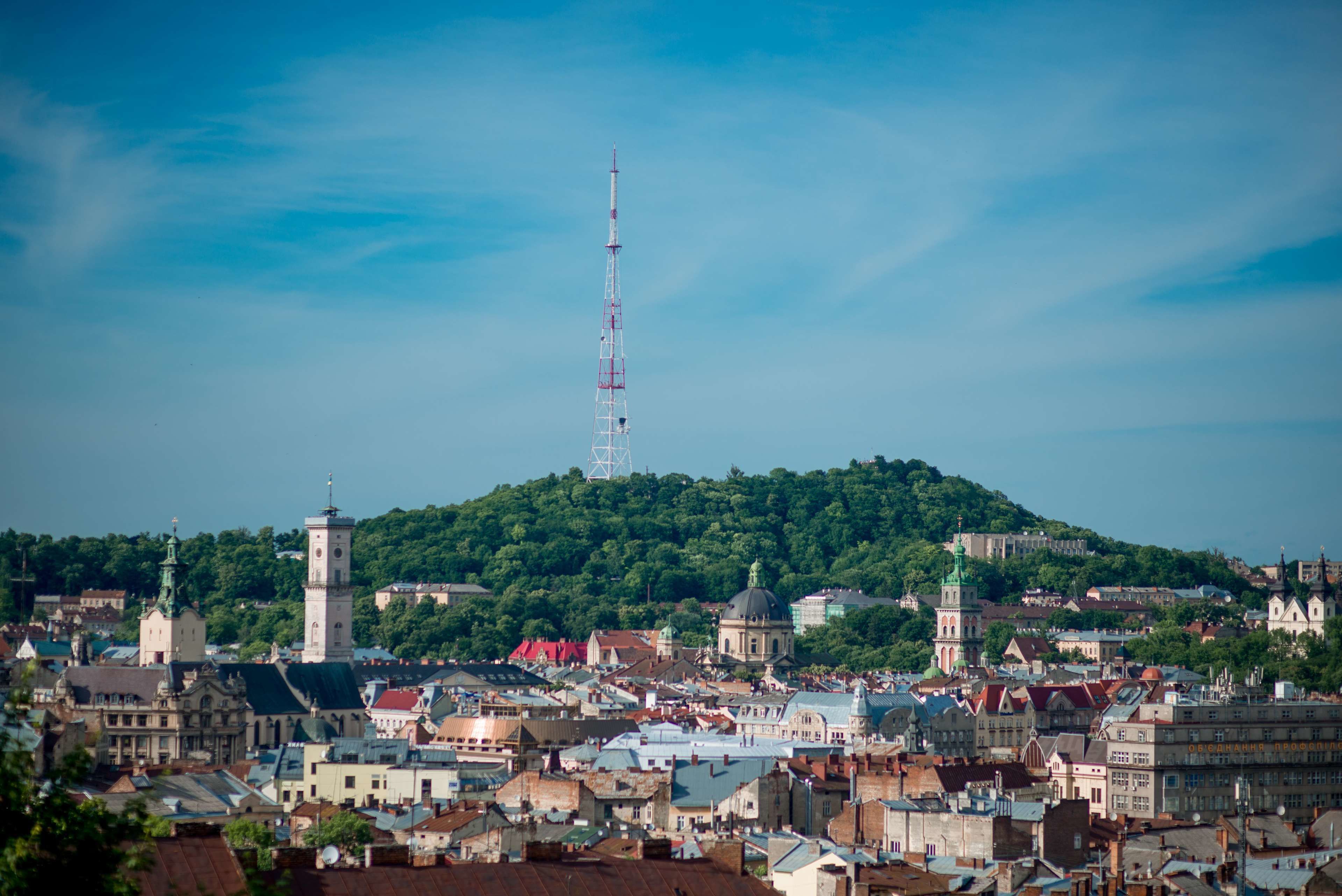 A cityscape with a prominent tower, historic buildings, and a hill with dense greenery.