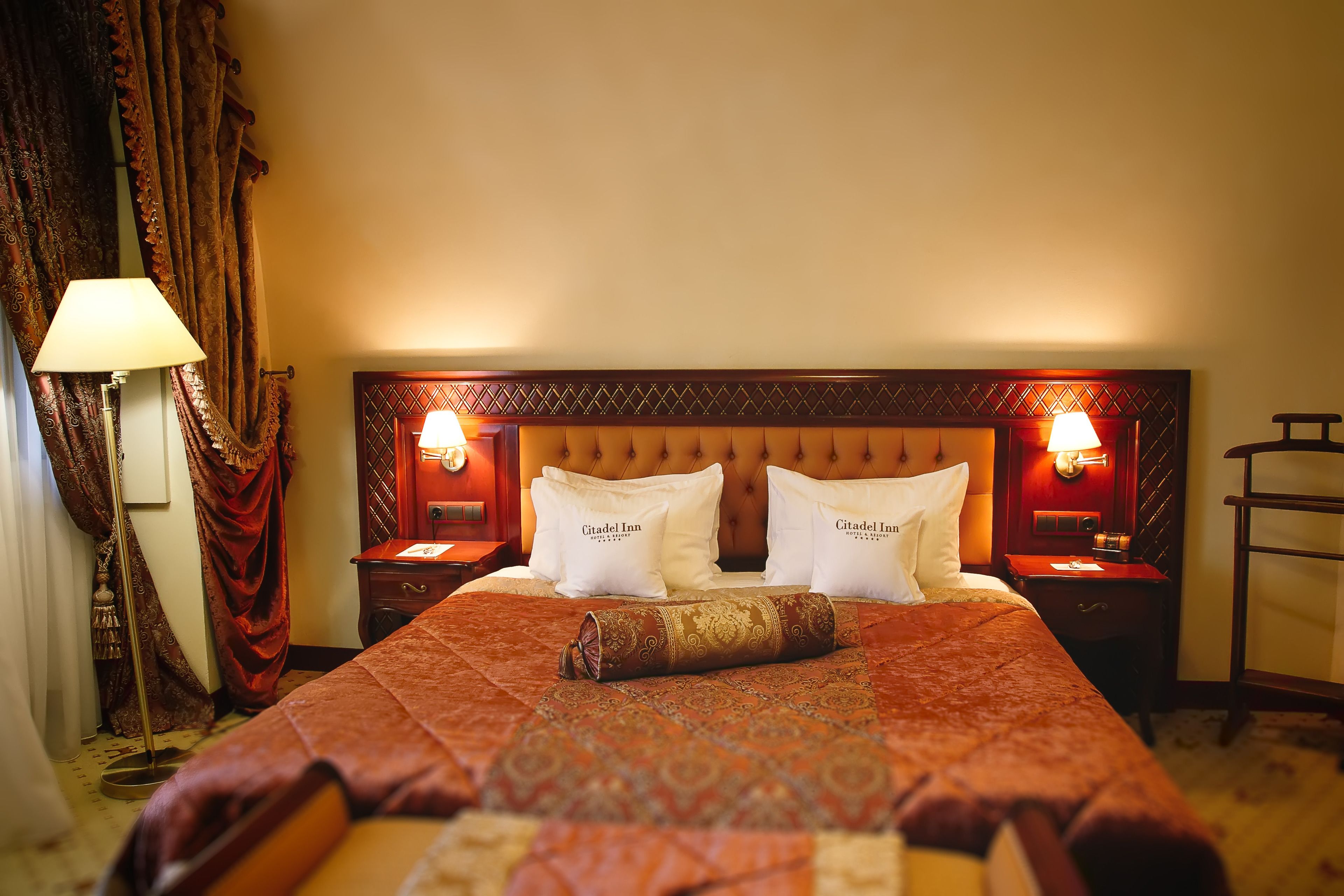 Una habitación de hotel con una cama grande, dos mesitas de noche, una lámpara y un cabecero con iluminación.