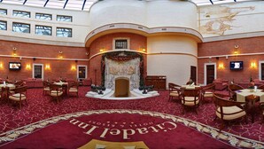 Een hotel lobby met een rood tapijt, meerdere zithoeken, een open haard en een grote muurschildering.