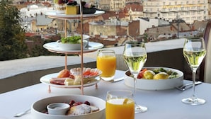 A table set with a three-tiered dessert stand, plates of food, glasses of orange juice, and wine glasses, overlooking a cityscape. - Citadel Inn Gastro Boutique Hotel (Lviv)