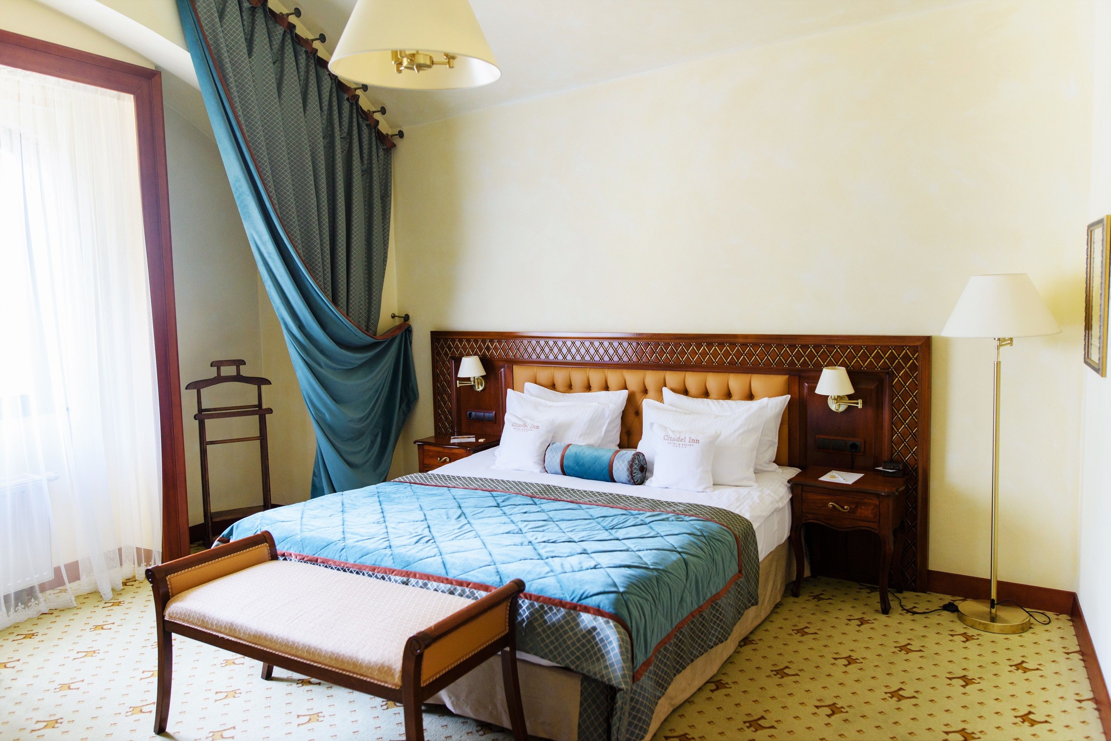 Ein Hotelzimmer mit Bett, Nachttisch, Stuhl, Lampe und einem Vorhangfenster.