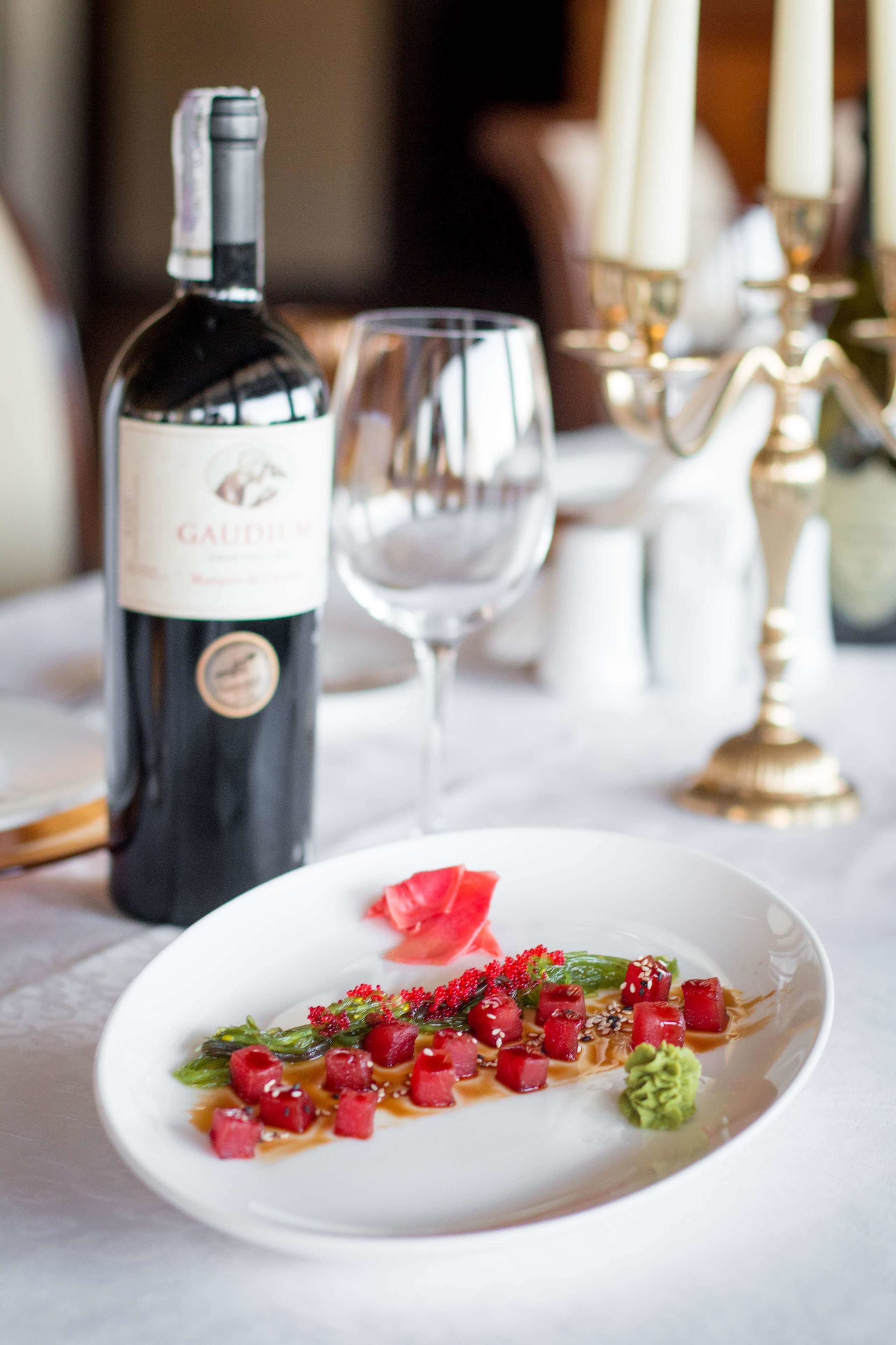 A dining table with a bottle of wine, a glass, and a plate of food.