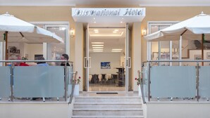 The entrance to an International Hotel with a glass door, a staircase leading up, and two white umbrellas on either side. - International Hotel (Rhodes)
