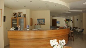A reception area with a curved wooden counter, a phone, and framed pictures on the wall. - International Hotel (Rhodes)