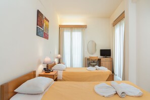 A hotel room with two beds, a desk with a chair, a television, and a painting on the wall. - International Hotel (Rhodes)