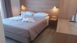 A hotel room with a bed, two pillows, a bedside table with a lamp, and a wooden nightstand. - International Hotel (Rhodes)