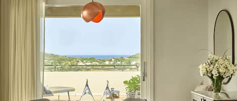 A dining area with a round table, chairs, and a view of the sea through a large window.