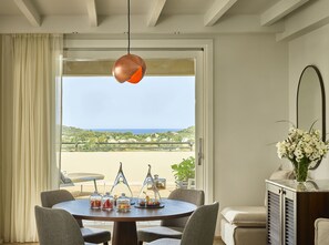 Ein Essbereich mit einem runden Tisch, Stühlen und Blick auf das Meer durch ein großes Fenster.