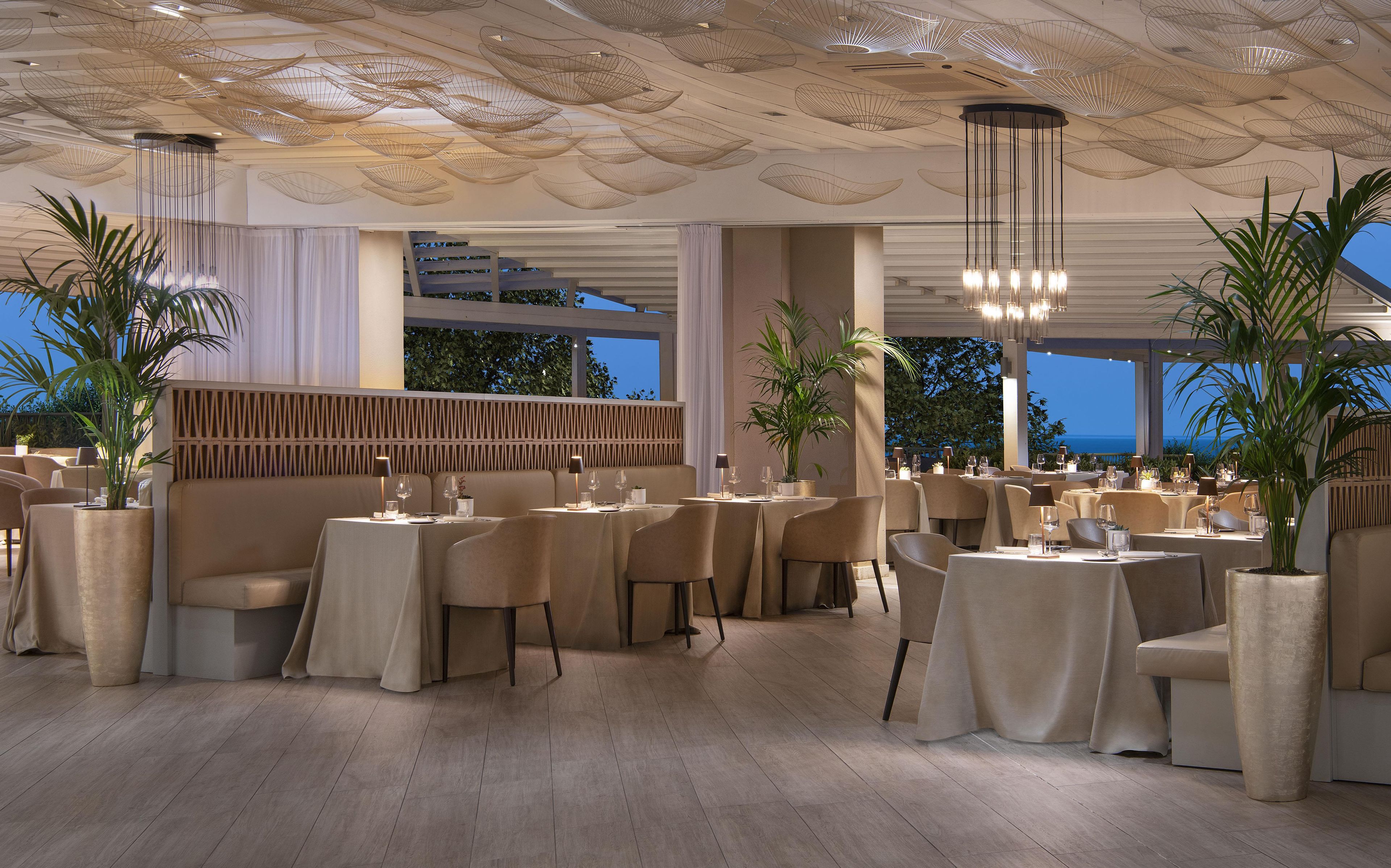 A restaurant with multiple tables, chairs, and hanging light fixtures.
