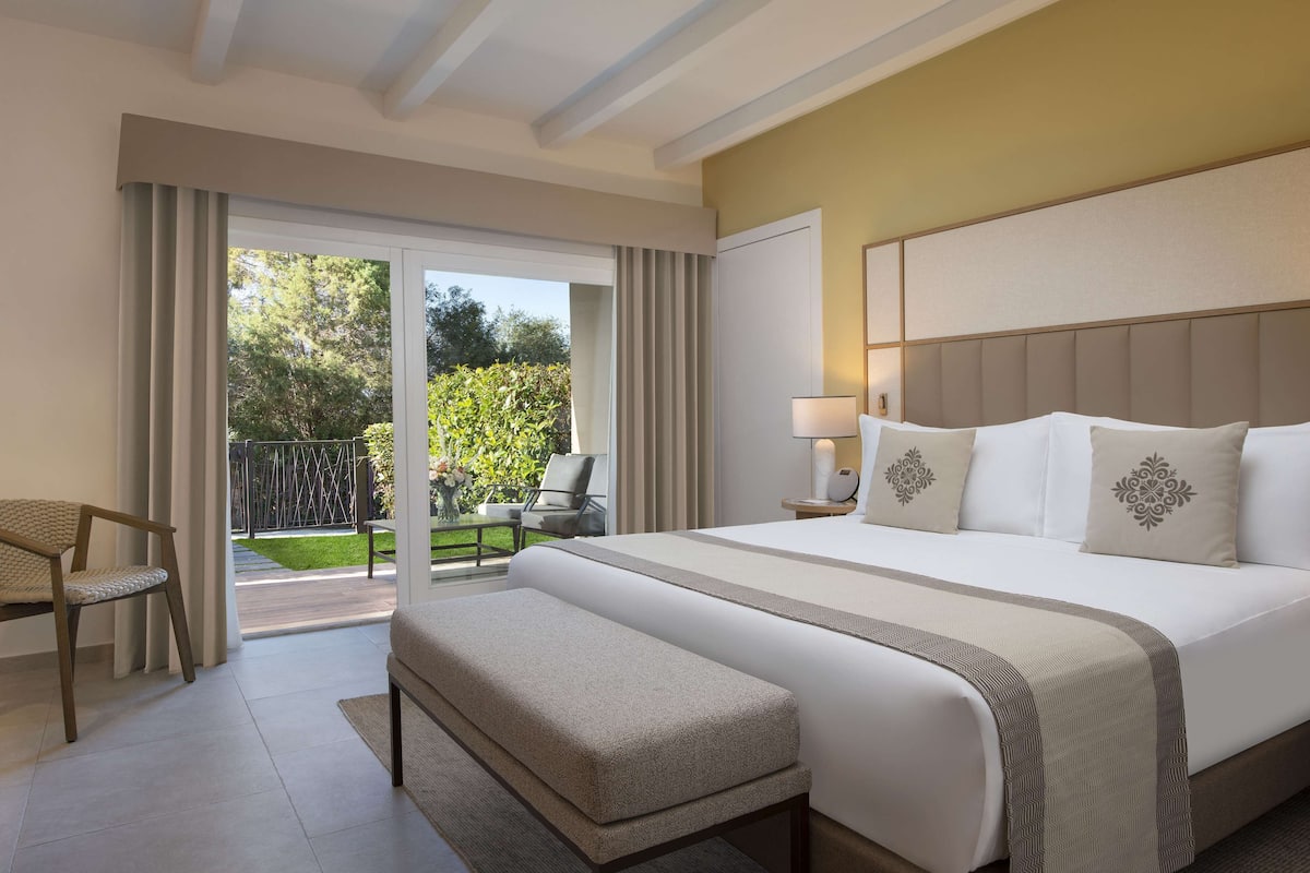 Een hotelkamer met een groot bed, een bankje, een stoel, een nachtkastje en uitzicht op de omgeving.