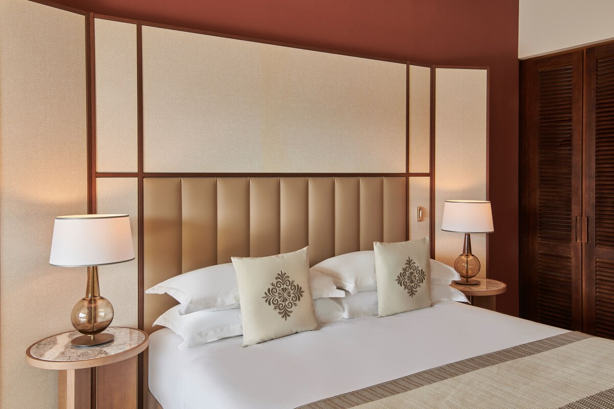 Een hotelkamer met een groot bed, twee nachtkastjes met lampen, een houten hoofdbord en een kledingkast.