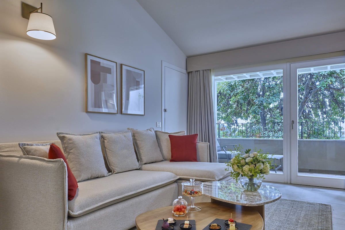 Een moderne woonkamer met een bank, een bijzettafeltje met desserts en uitzicht op groen.