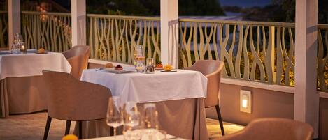 An outdoor dining area with tables set for two, featuring white tablecloths and candle centerpieces.