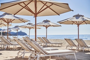 Une plage bordée de rangées de chaises longues et de grands parasols.