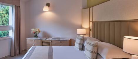 Een verzorgde hotelkamer met een groot bed, bedlampen, een nachtkastje en een raam met gordijnen.