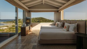 Ein Schlafzimmer mit großem Fenster, einem Bett, einem Fernseher und Blick auf eine grüne Landschaft.