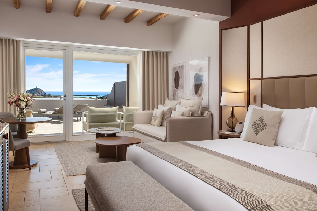Een hotelkamer met een groot bed, een slaapbank, een eettafel en uitzicht op de oceaan door de schuifdeuren.