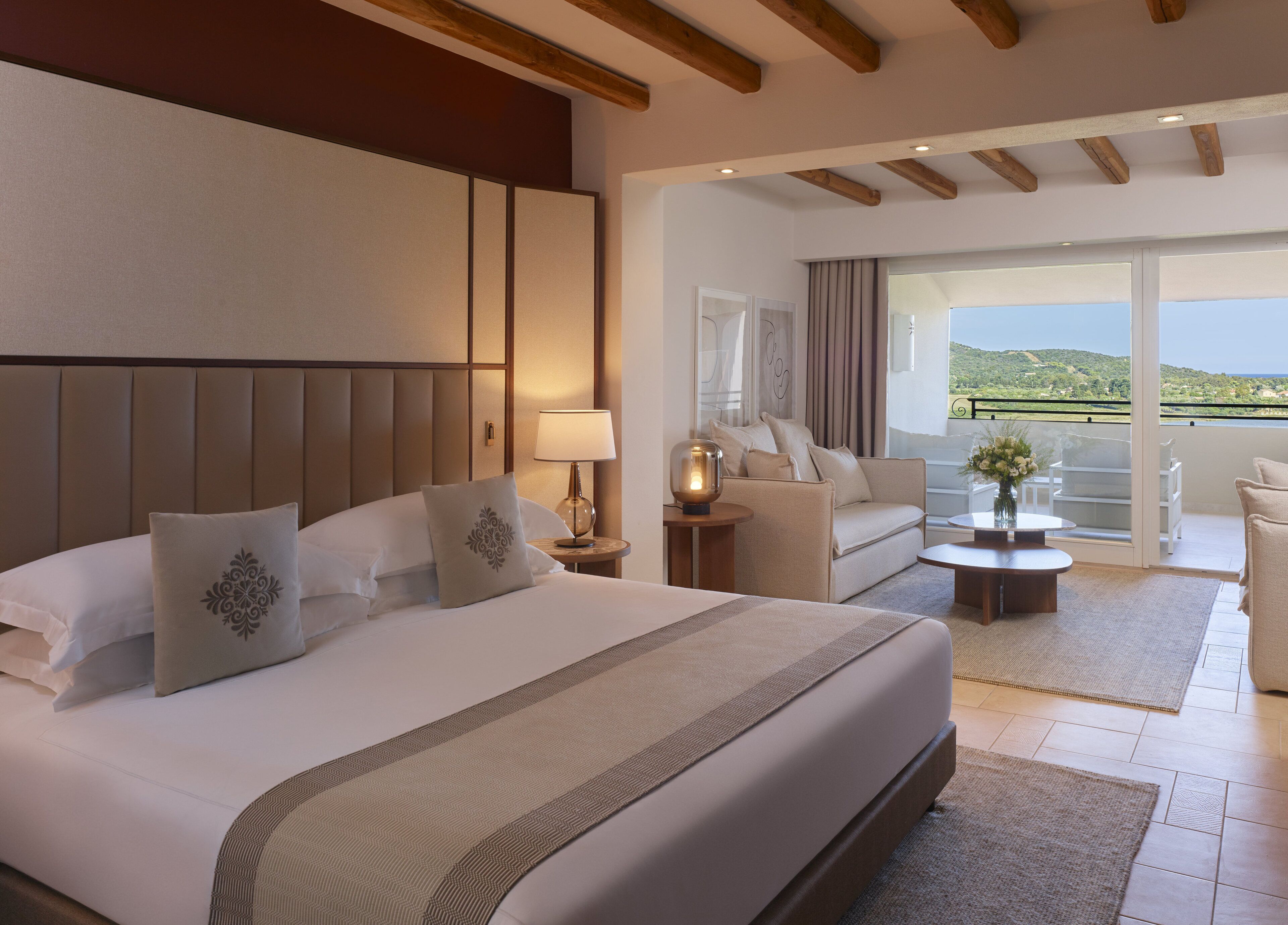 A hotel room with a large bed, a sofa, a coffee table, and a balcony with a view.