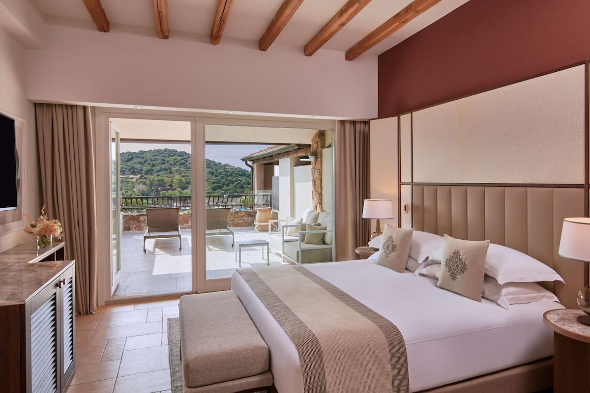Een hotelkamer met een groot bed, een televisie, een bureau en een balkon met buitenmeubels.
